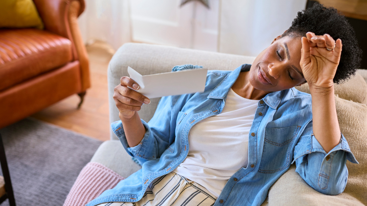 A Black woman reclines on a couch while fanning herself during a hot flash.