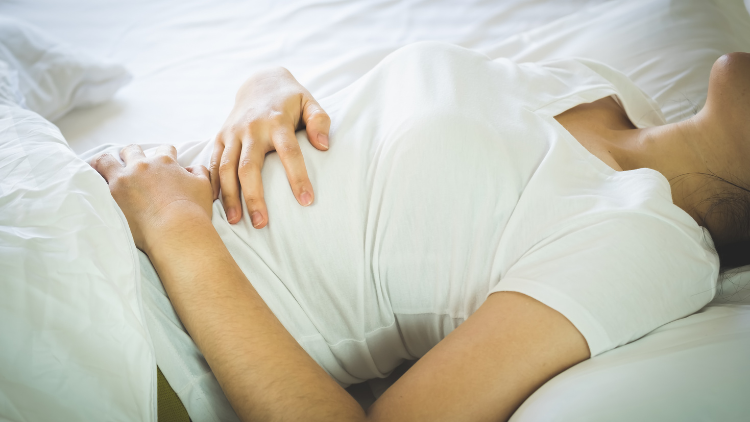A woman clutches her abdomen as she experiences inflammation and discomfort.
