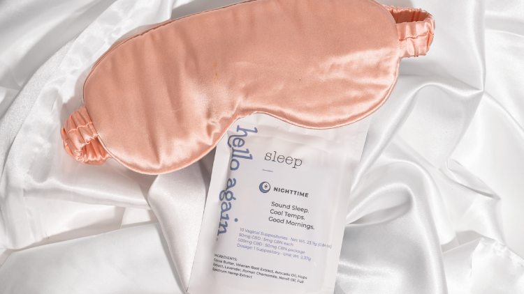 Pink sleep mask and Hello Again Sleep product lying on white satin sheets.