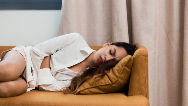 Woman on brown couch with cramps two weeks before your period.