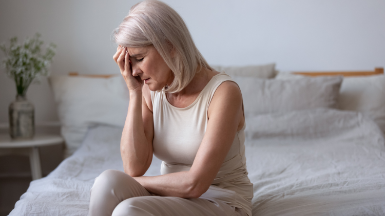 Woman holding her head while sitting on a bed
