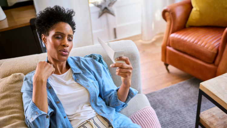 A Black woman fans herself with a piece of paper during a hot flash.