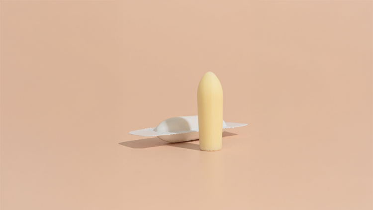 Vaginal suppository standing upright beside a suppository shell.