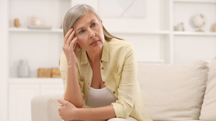 Woman sitting on couch looking fatigued and thoughtful, illustrating symptoms addressed by CBD for Perimenopause and Menopause such as brain fog and stress.