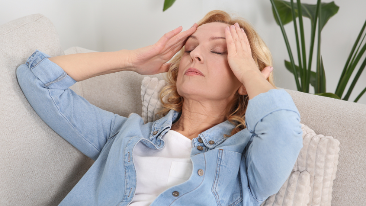 Woman holding her head with eyes closed, showing how hormones affect women through stress, headaches, and mental fatigue