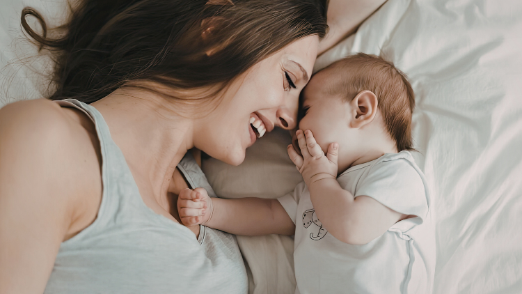 Mother lying beside her giggling baby, illustrating the protective bond often associated with a matriarch in nature and family life.