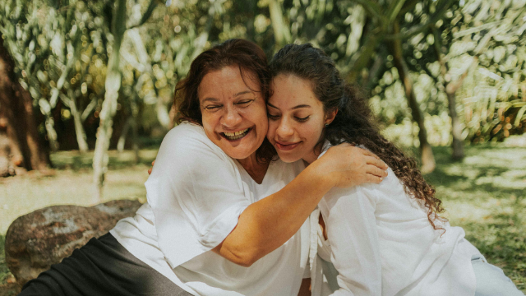 Older woman embracing a younger woman outdoors, symbolizing the wisdom and connection of a matriarch across generations.