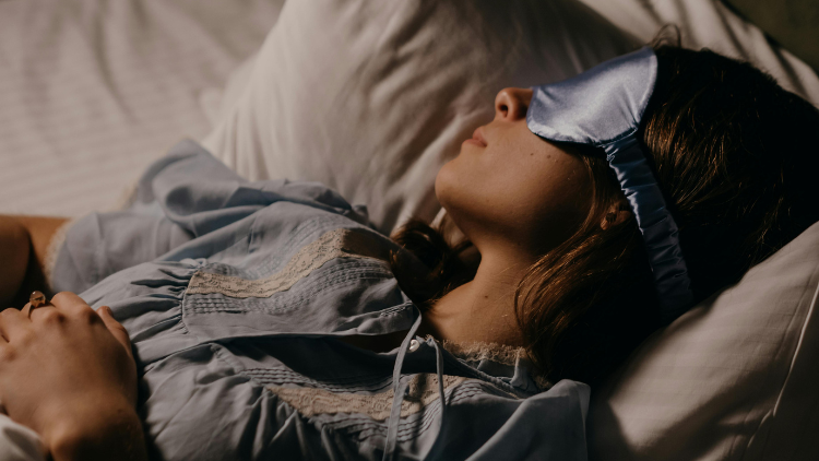 Woman sleeping peacefully with a satin sleep mask, illustrating the benefits of CBN for sleep and nighttime relaxation.