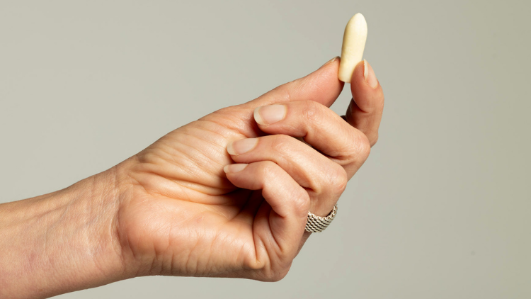 A hand holding a Hello Again vaginal suppository designed for targeted cannabinoid support.