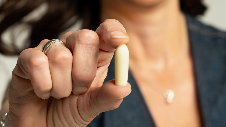 A woman holding a Hello Again vaginal suppository, showing the simple size and format of suppositories for women.